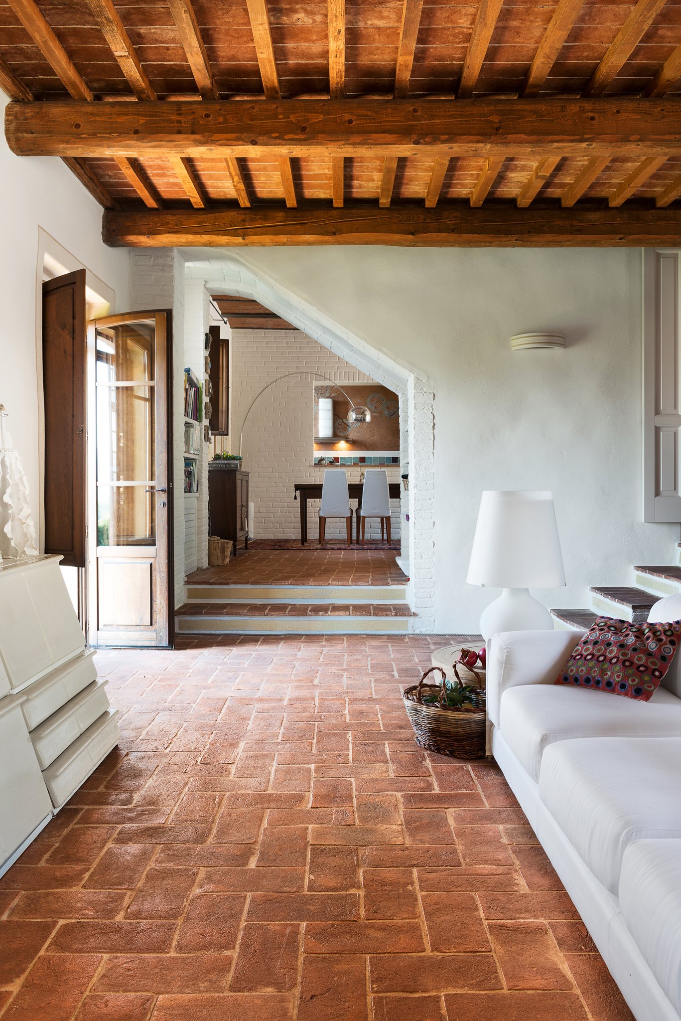 Living con cotto, travi, arco in muratura e scala